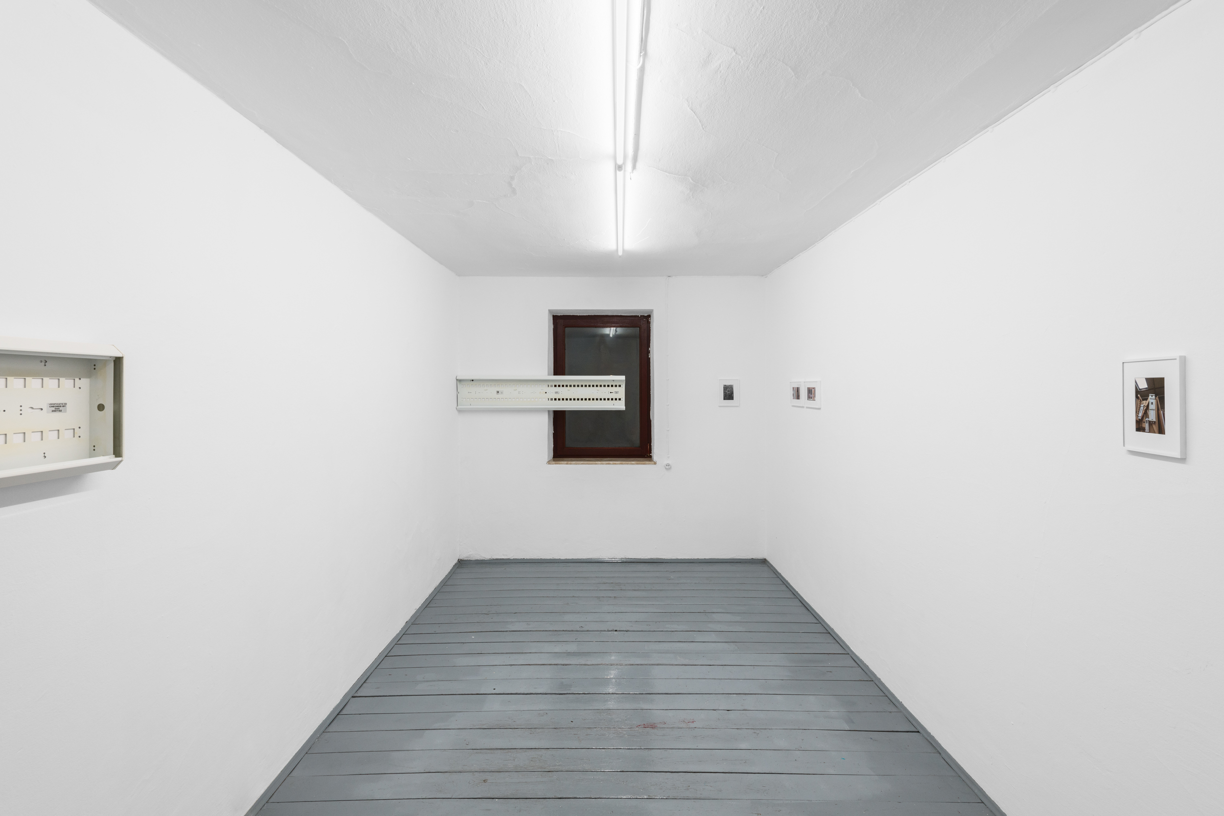Aisha Altenhofen solo exhibition at Austin Space: Installation view of a minimal white gallery space with grey wooden floors, featuring small framed photographic works and a horizontal industrial light fixture mounted across a central window.