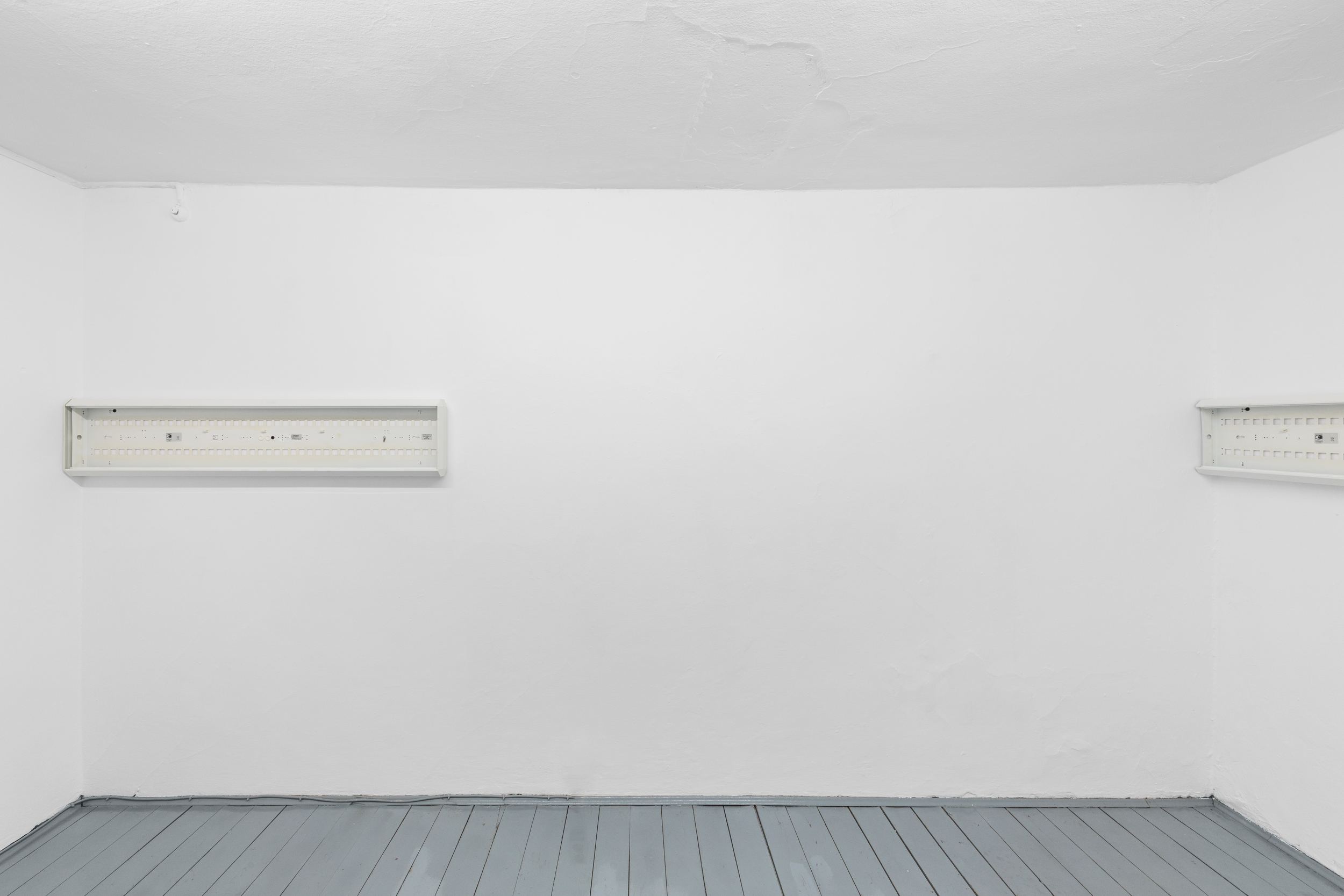 Aisha Altenhofen solo exhibition at Austin Space: Installation view of two white grid light fixtures installed at the wall, with an empty white wall between them.