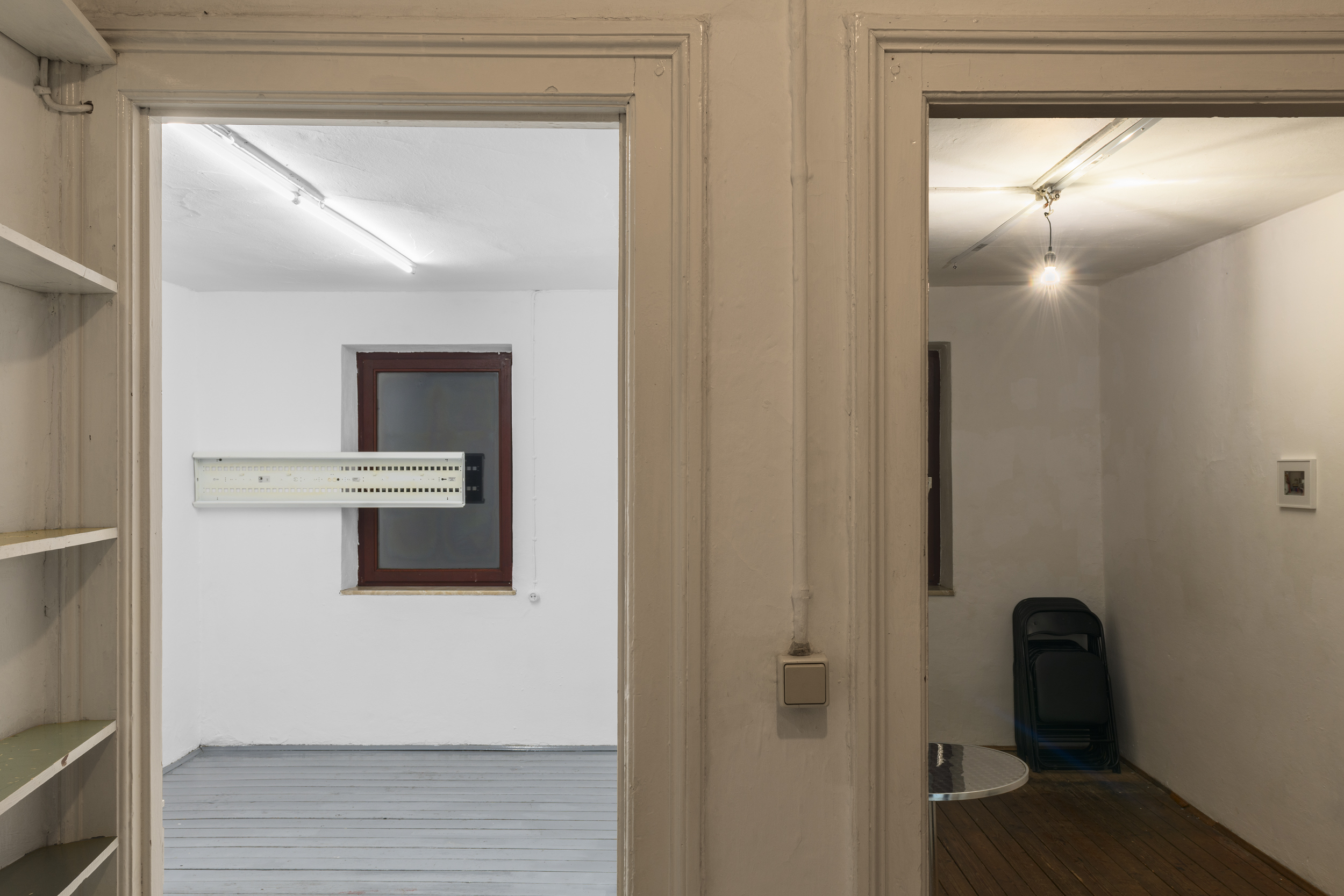 Aisha Altenhofen solo exhibition at Austin Space: View from outside the two gallery rooms, one in white gallery lighting and grey floors, the other in warm light and brown unpainted floors.