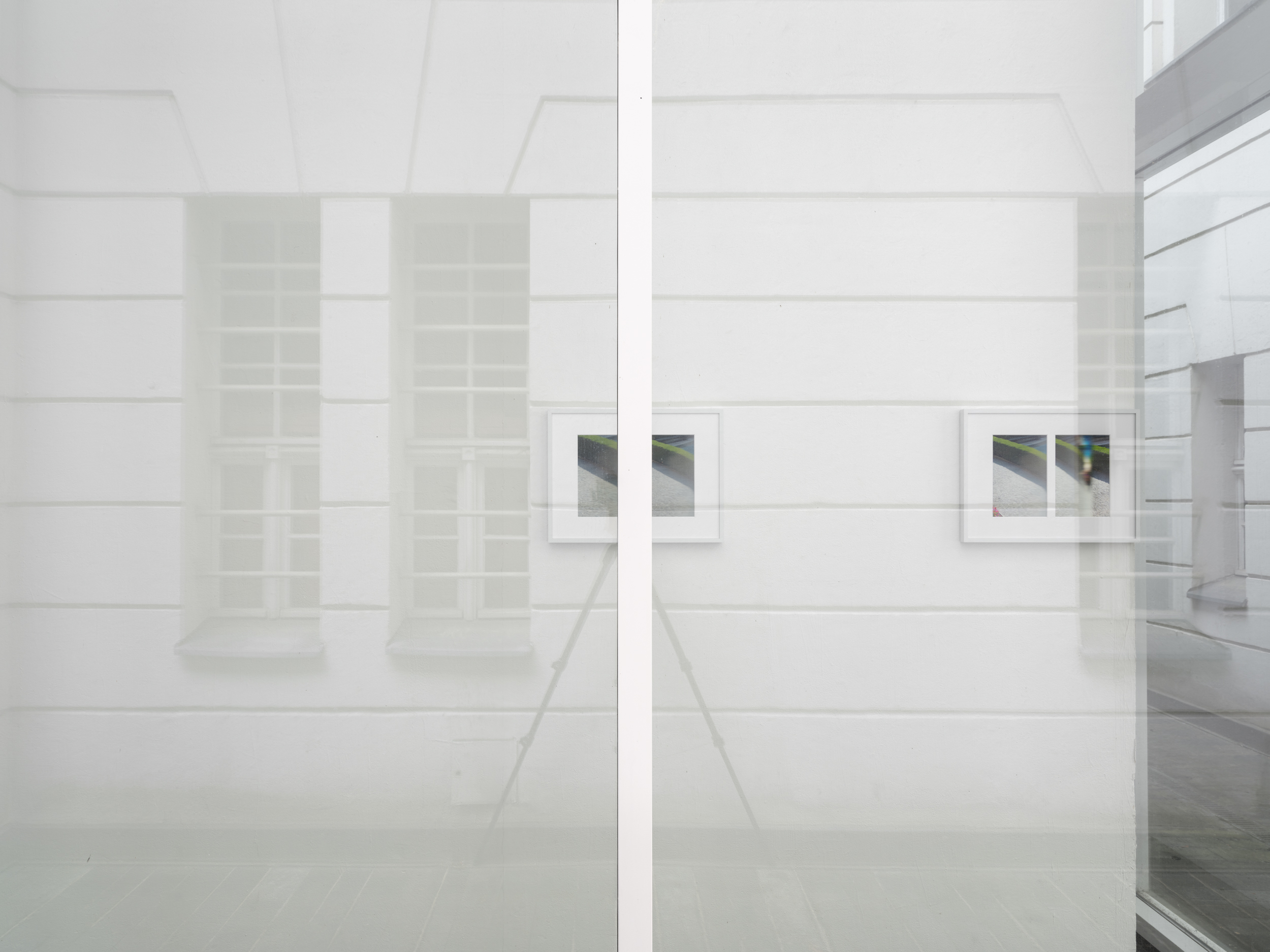 Aisha Altenhofen solo exhibition at Austin Space: Installation view towards the door with a warmer light temperature, a small photographic work hangs on the opposite wall to a grid light fixture that is hung on the wall.