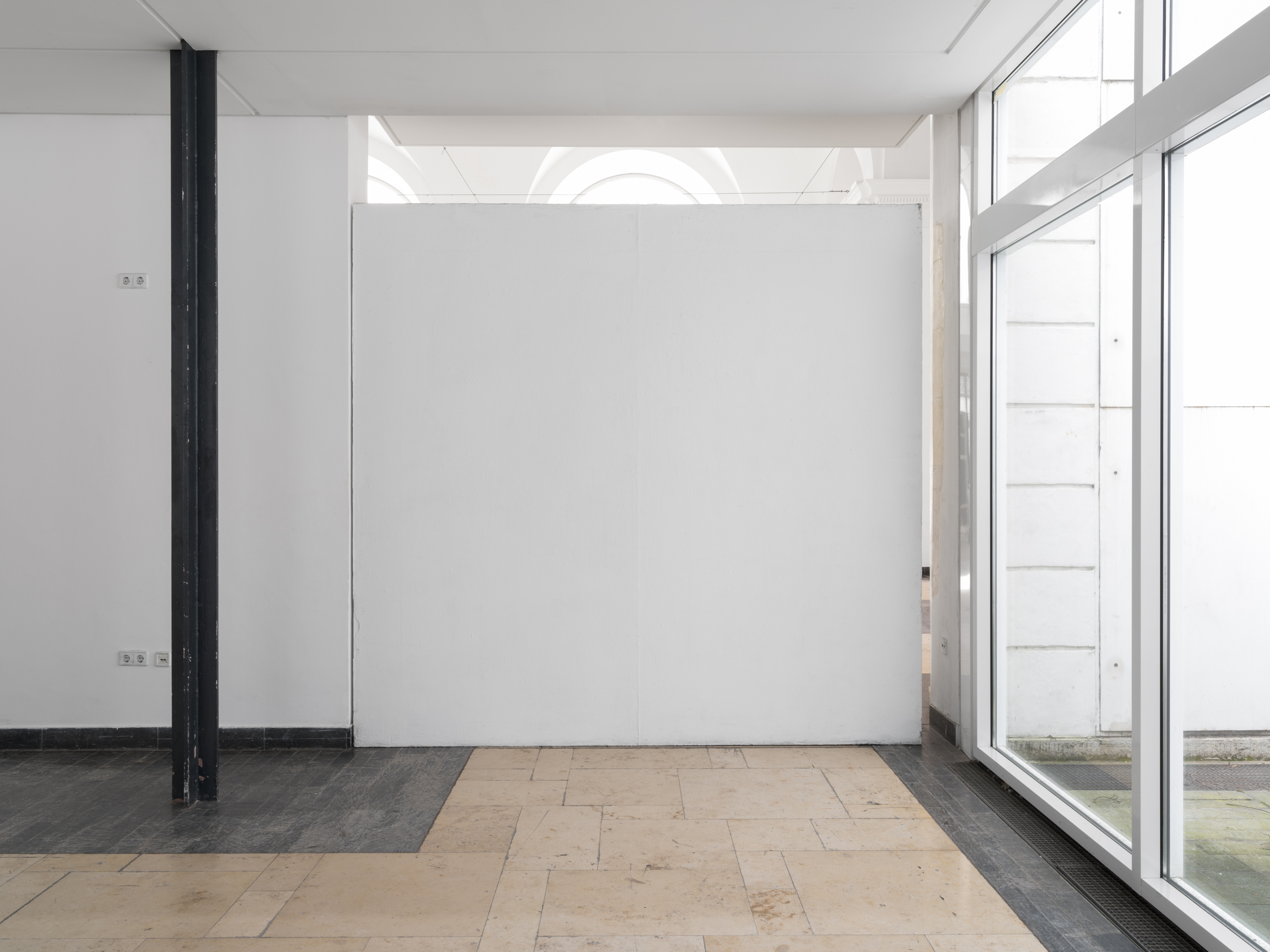 Aisha Altenhofen solo exhibition at Austin Space: View from outside the two gallery rooms, one in white gallery lighting and grey floors, the other in warm light and brown unpainted floors.